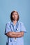 Elderly physician assistant with stethoscope standing with arm crossed in studio