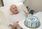 Elderly retired family physician with a thumbs up signal for his 89th birthday cake delivered to his bedside.