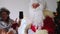 Elderly santa claus with his wife congratulates children and adults, shows phone with blank black screen, concept of christmas,