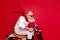 Elderly santa man moving fast to party by vintage moped wear white jumper and trousers  red background