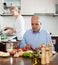 Elderly senior preparing vegetarian food and mature wife doing