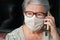 Elderly senior woman with glasses wearing hand made cotton mouth nose virus face mask, talking over her phone. Coronavirus covid-