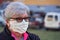 Elderly senior woman wearing home made cloth face mouth nose virus mask outside, blurred buildings and cars background. Can be