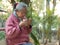 Elderly sits at balcony in garden enjoy hot beverage.