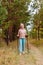 Elderly sixty-year-old woman in sportswear is engaged in Nordic walking with sticks in the forest in the autumn