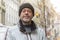 An elderly and smiling bearded man 50-55 years old in a hat against the backdrop of a European city.