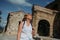 Elderly smiling senior traveling woman backpacker tourist walking posing outdoors in ancient Europe fortress ruins