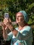 Elderly smiling woman makes selfie on smartphone in summer sunny day