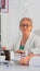 Elderly specialist doctor in lab coat typing on laptop and smiling at camera