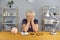 Elderly tired woman sitting with notes, calculator and piggybank and covering stressed face with hands