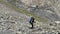 An elderly tourist with a large backpack walks along a stone mountain path. Climbing Kazbek from the north