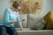 Elderly upset woman examines stains on sofa with magnifying glass