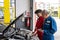 Elderly vehicle mechanic holding tablet maintenance the automotive engine in an auto repair service center