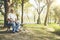 Elderly, visually impaired Asian man wearing dark glasses using a cane for the blind sits alone in a wooden chair in a park.