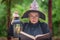 An elderly witch in glasses in the woods, holding an open book, illuminating it with an antique lamp
