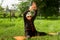 An elderly woman of 90 years old, with gray hair and a headband, doing fitness in the garden on a yoga mat