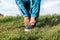 An elderly woman adjusts her sports shoes on her foot while standing on the grass. Close-up. The concept of an active