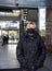 An elderly woman in a black jacket and a black medical mask walks out of the door of a shopping center