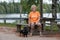 Elderly woman with black and tan dachshund sits on park bench by lake in summer