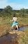 Elderly woman crossing a small stream on stones, hiking in the Sierra Norte de Sevilla Natural Park, Spain