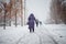 elderly woman in dark coat walks along road that is not snowed off in the city. Poor utilities work. Not working snow equipment.