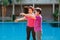 Elderly woman doing exercise with daughter at pool patio