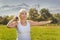 Elderly woman is engaged in fitness with a dumbbell in isolation mode outdoors in a park against a background of mountains