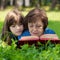 Elderly woman and girl are lying on the lawn, embracing and reading a book against green nature background.