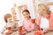 Elderly woman and happy grandson and granddaughter drink tea from red mugs in kitchen.