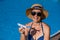 An elderly woman in a hat and sunglasses holds a model airplane while sitting by the pool. Retirement vacation concept.