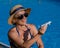 An elderly woman in a hat and sunglasses holds a model airplane while sitting by the pool. Retirement vacation concept.