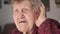 Elderly woman with a hearing aid device in her ear talks and tries to listen