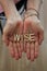 An elderly woman with her hands together with wooden letters forming the word Wise