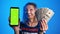 Elderly woman holding phone with green screen in one and money in another hand. Lottery win