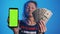 Elderly woman holding smartphone with green screen and money. Investment app