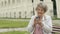 Elderly woman holds silver mobile phone outdoors