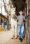 Elderly woman horse breeder leading white racehorse along stables outdoors