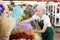 Elderly woman, hostess of the flower market, collects Ruscus Italie in bouquet