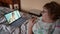 An elderly woman lies in bed and having an online consultation with a doctor on a laptop.