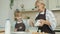 Elderly woman and little girl in aprons cooking in kitchen adding flour to dough and talking