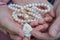 An elderly woman and a little girl are holding a beautiful white rosary. Hands of an old woman and a little girl with pearl rosary