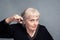 An elderly woman with a pair of scissors in her hand on a gray background. Barber services