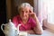 Elderly woman pensioner sitting at a table in the kitchen in his house