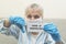 Elderly woman with protective mask holding a paper with a positive result on coronavirus. Sick granny looking into camera showing