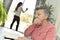 Elderly woman reading a book with a home carer in the background