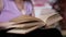 Elderly Woman Reading a Book, Turning the Pages in the Rays of Sunlight Indoors