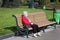 An elderly woman in a red jacket sits on a bench in a park.