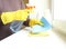 An elderly woman`s gloved hands hold a cleaning agent and sponge for cleaning Windows and frames