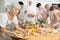 Elderly woman seasoning dish with sauce during group cooking class