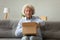 Elderly woman sitting on couch unpacking parcel feels satisfied